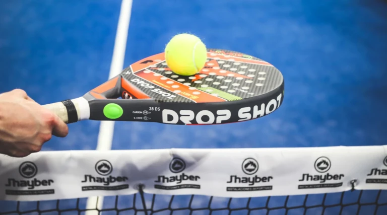 En närbild av ett padelracket som träffar en gul tennisboll över ett nät.