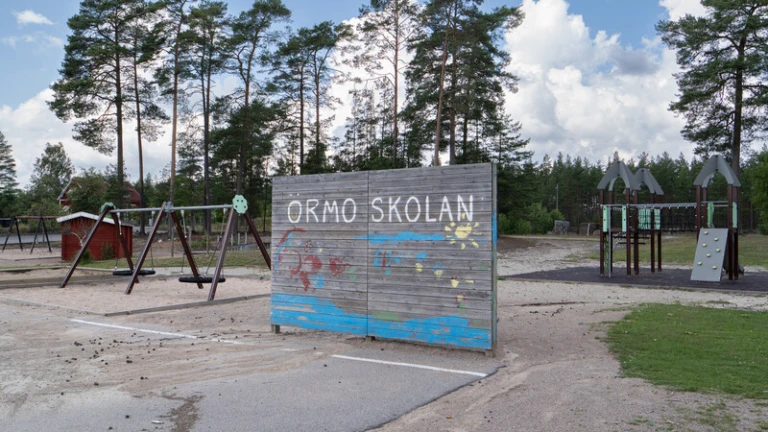 Skolgård meed sand, gräs och ett bollplank.