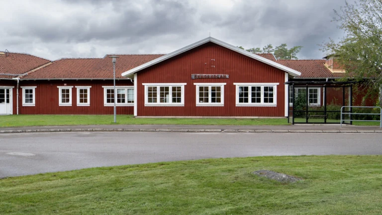Röd skolbyggnad, gräs och asfalt.
