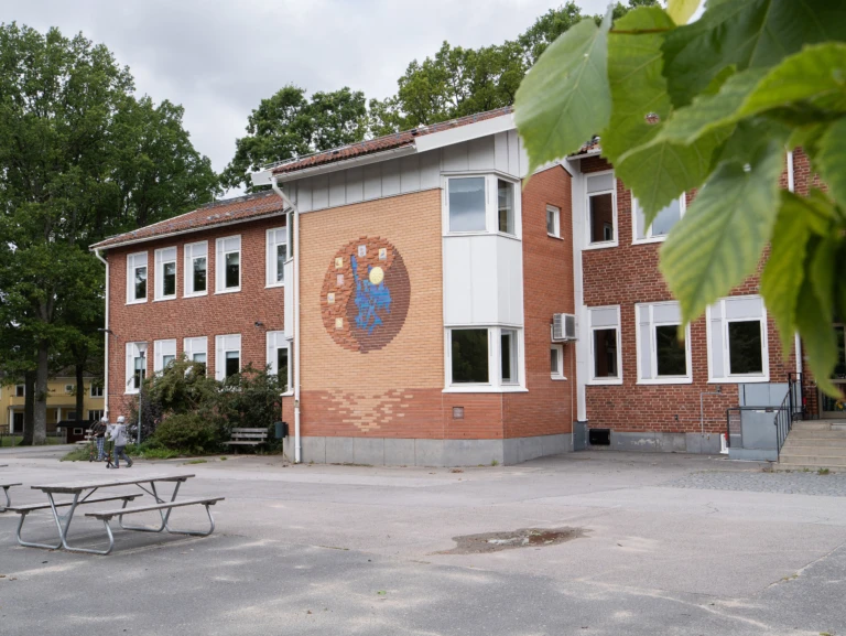 Urshultsskolans röda tegelbyggnad, asfalt och träd i förgrunden