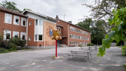 Skolbyggnad i rött tegel med asfalt i förgrunden.