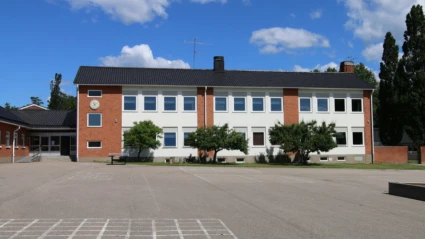 Skolbyggnad i rött tegel med asfalterad skolgård i förgrunden