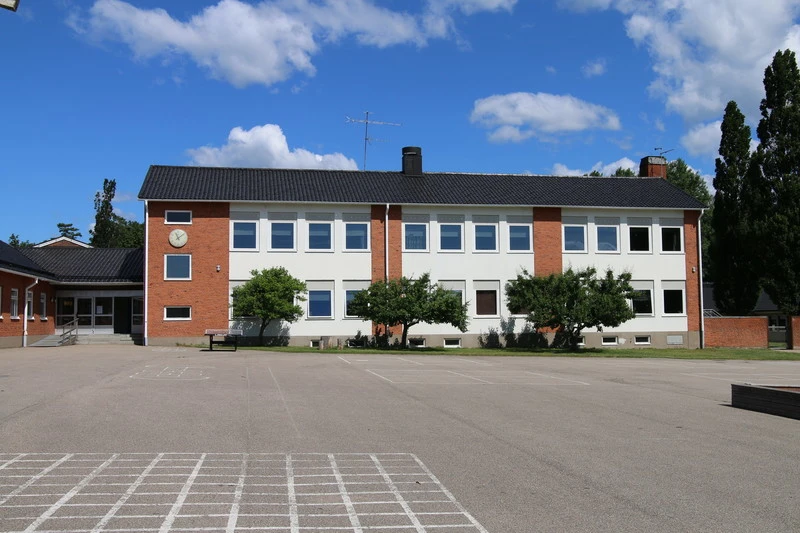 Asfalterad skolgård och skolbyggnad i rött tegel.