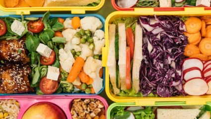 Färgglada matlådor fyllda med olika nyttiga livsmedel, inklusive sallad, tomater, morötter, blomkål, ärtor, rödkål, rädisor, nötter, frukt och smörgåsar.