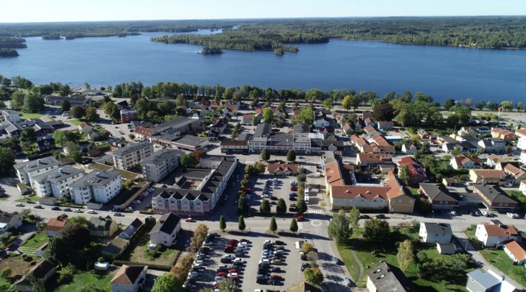 Flygbild över Tingsryd med bostadsområden, parkeringsplatser och grönområden, beläget vid en stor sjö med flera små öar i bakgrunden.