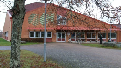 Wasaskolans entré till en tegelbyggnad med rött tak, stora fönster och en gångväg som leder fram till dörrarna. Några cyklar står parkerade utanför, och träd med höstlöv ramar in bilden.